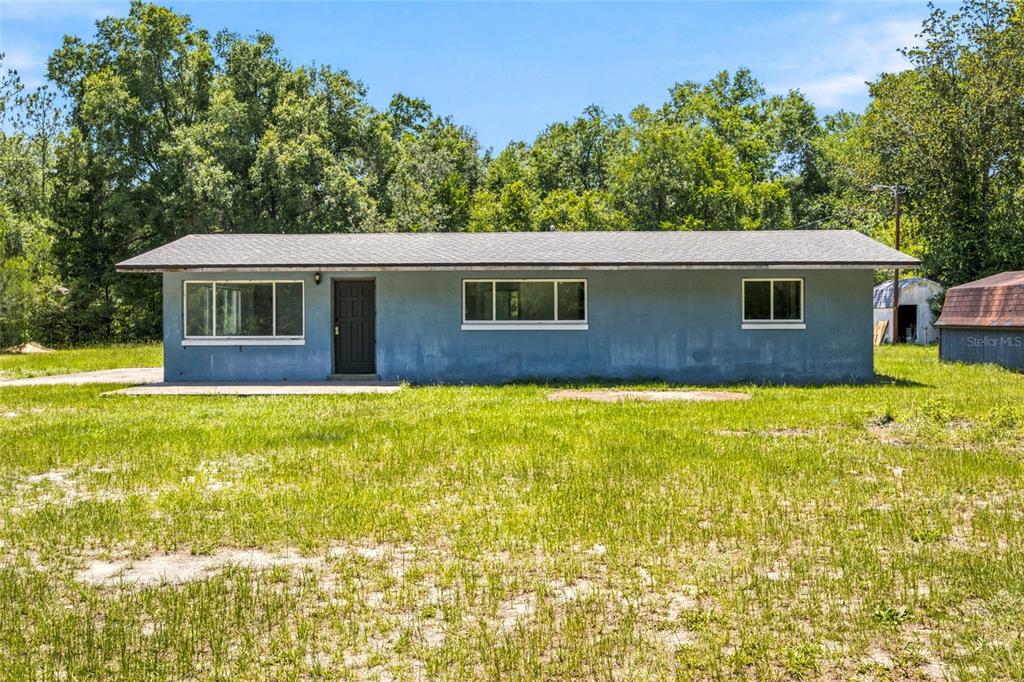 A single-story blue house with a dark door and three windows sits on a grassy lot — 14600 NE 150TH AVENUE, FORT MC COY, FL