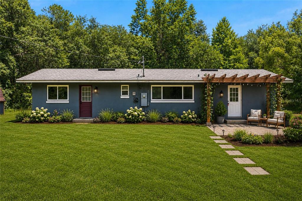 A gray, single-story house features a wooden pergola over a patio and a green lawn — 14600 NE 150TH AVENUE, FORT MC COY, FL