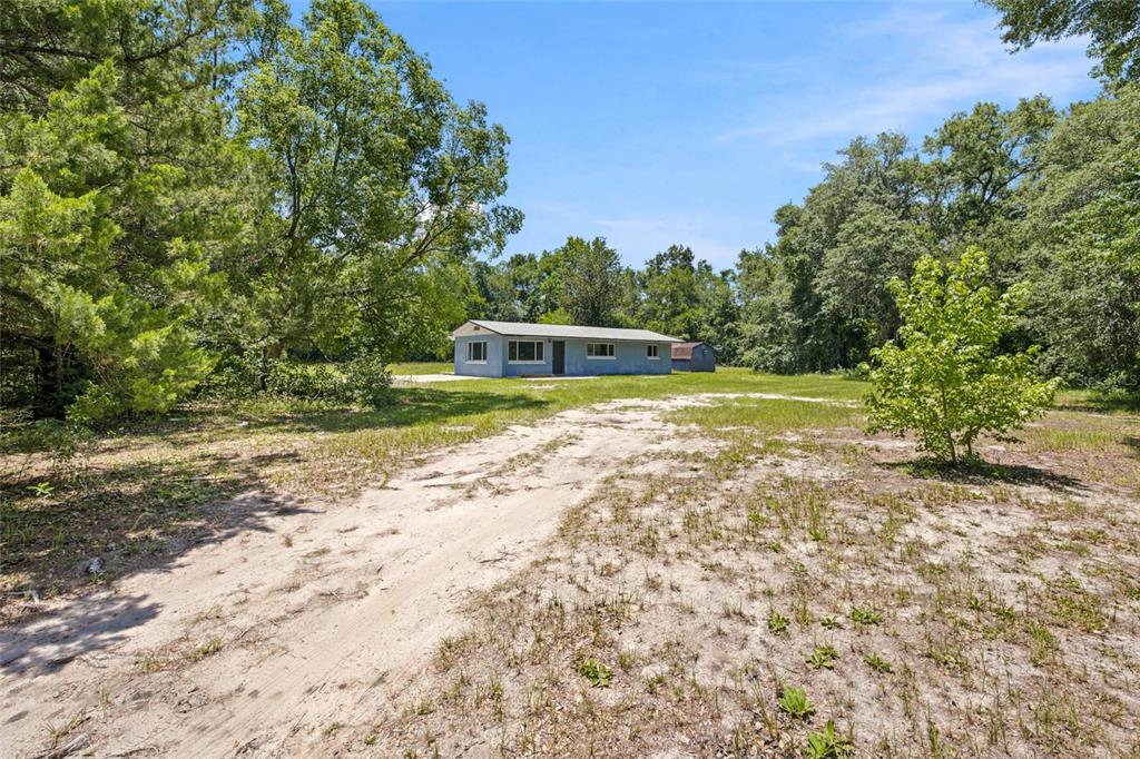 A single-story light blue house sits on a large, sandy lot surrounded by trees — 14600 NE 150TH AVENUE, FORT MC COY, FL