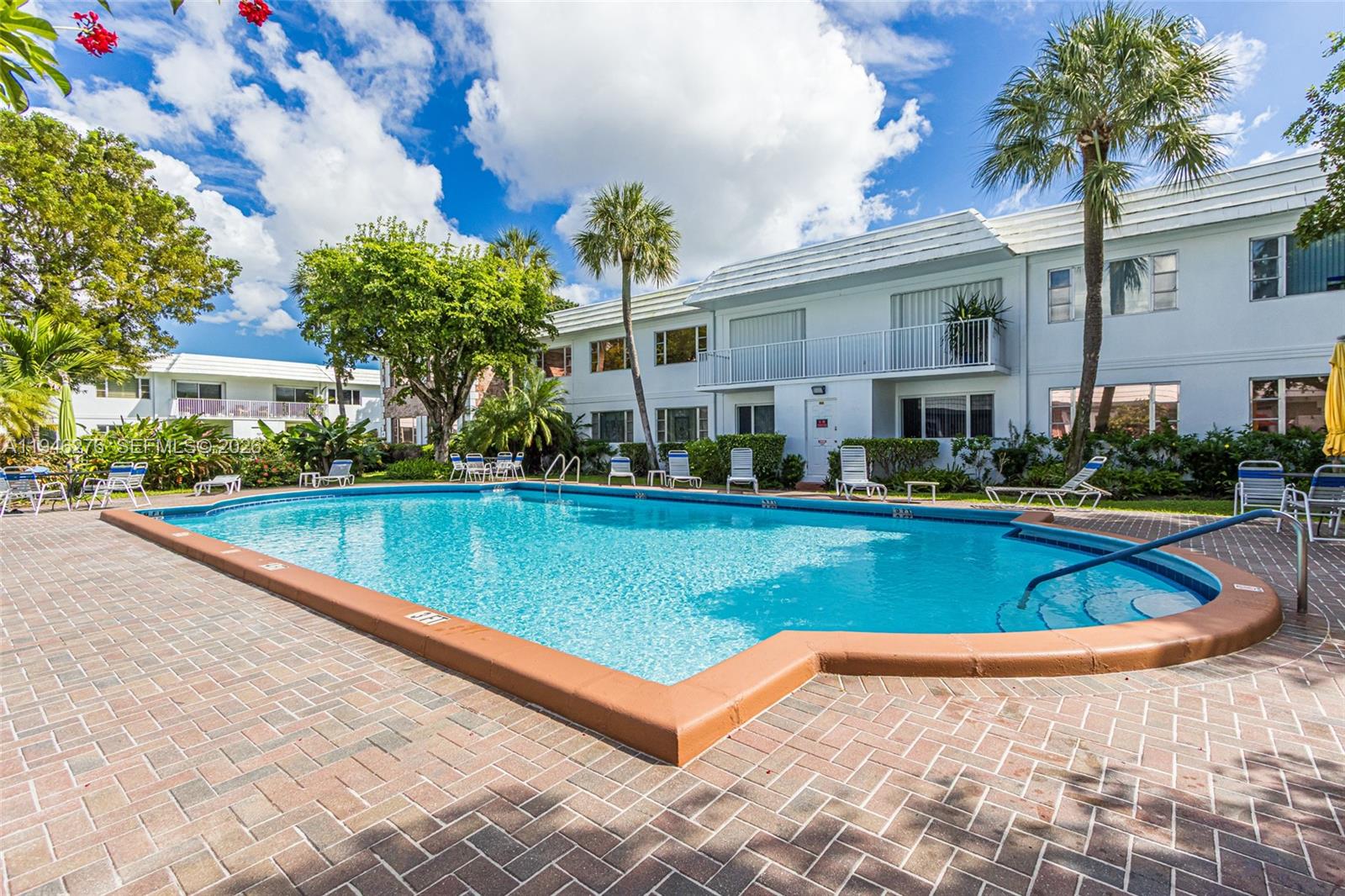 A swimming pool with a brick deck sits in front of a two-story apartment building — 412 S Cypress Rd # 222, Pompano Beach FL 33060, POMPANO BEACH, FL