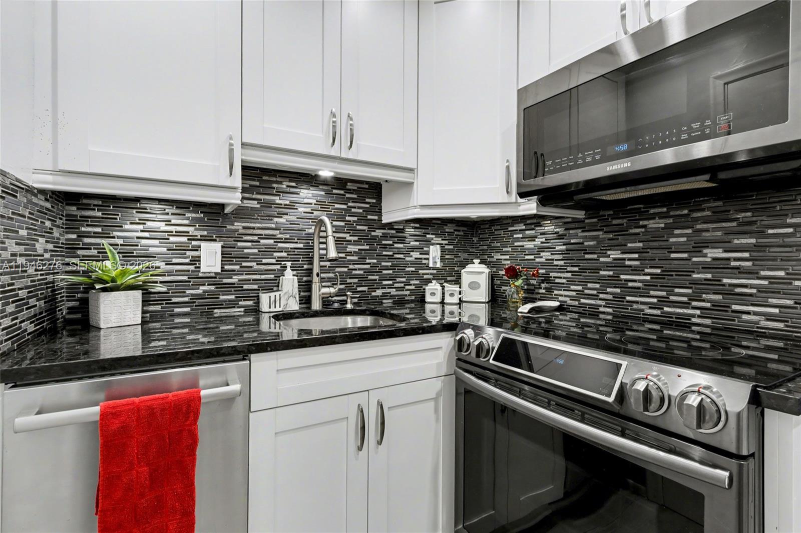 A kitchen features white cabinets, black granite countertops, a stainless steel stove, and tiled backsplash — 412 S Cypress Rd # 222, Pompano Beach FL 33060, POMPANO BEACH, FL