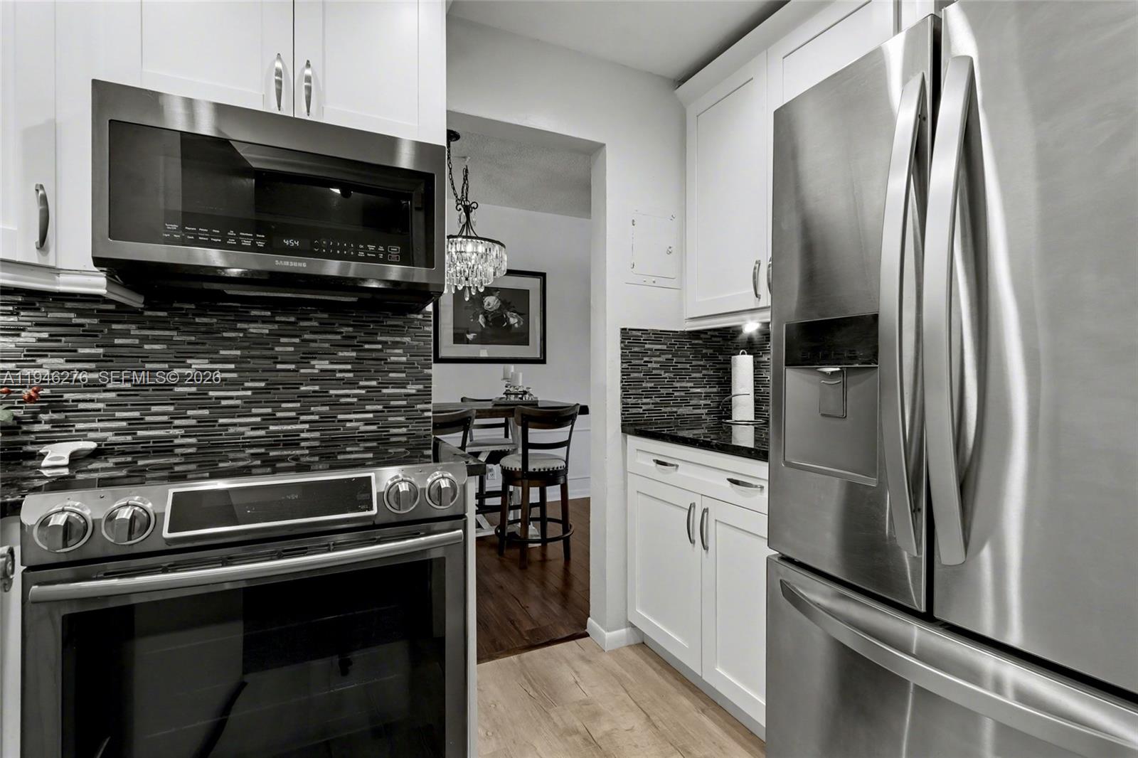 A kitchen features white cabinets, stainless steel appliances, and a dark mosaic tile backsplash — 412 S Cypress Rd # 222, Pompano Beach FL 33060, POMPANO BEACH, FL