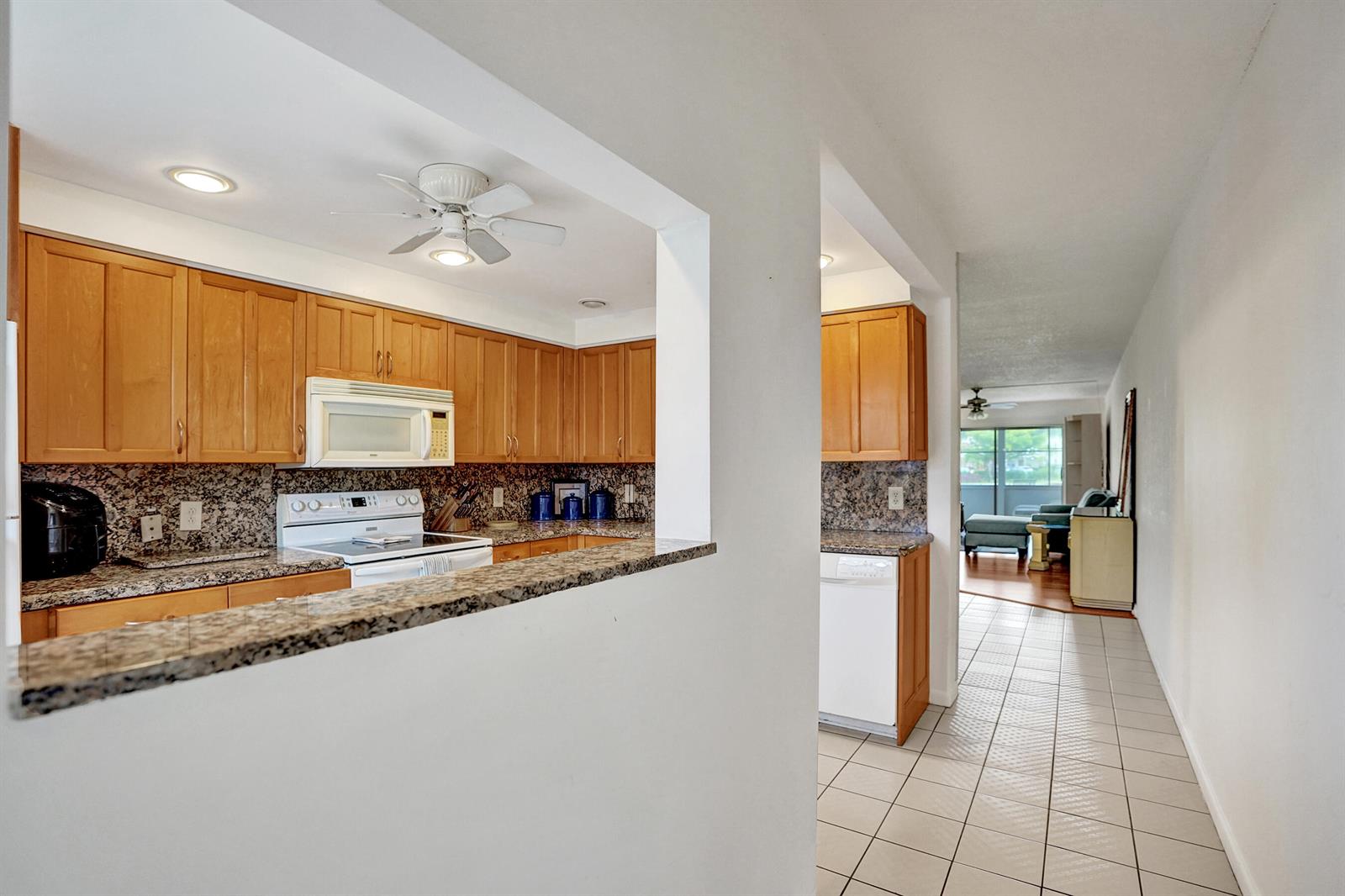 A kitchen with wood cabinets and granite countertops opens to a tiled hallway and living area — 1020 Lincoln, Boca Raton FL 33434, BOCA RATON, FL