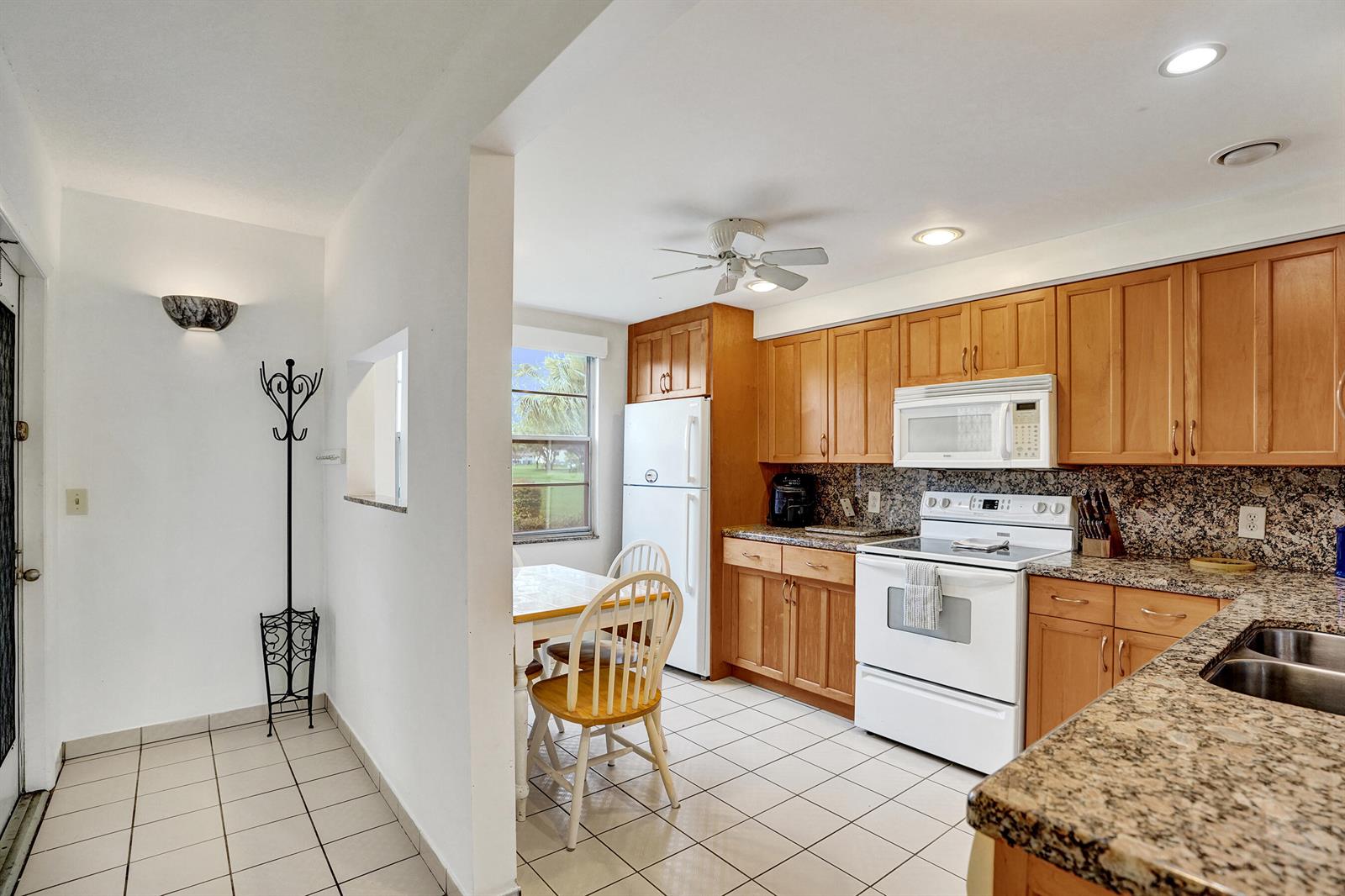 A kitchen features light wood cabinets, granite countertops, white appliances, and a small dining area — 1020 Lincoln, Boca Raton FL 33434, BOCA RATON, FL