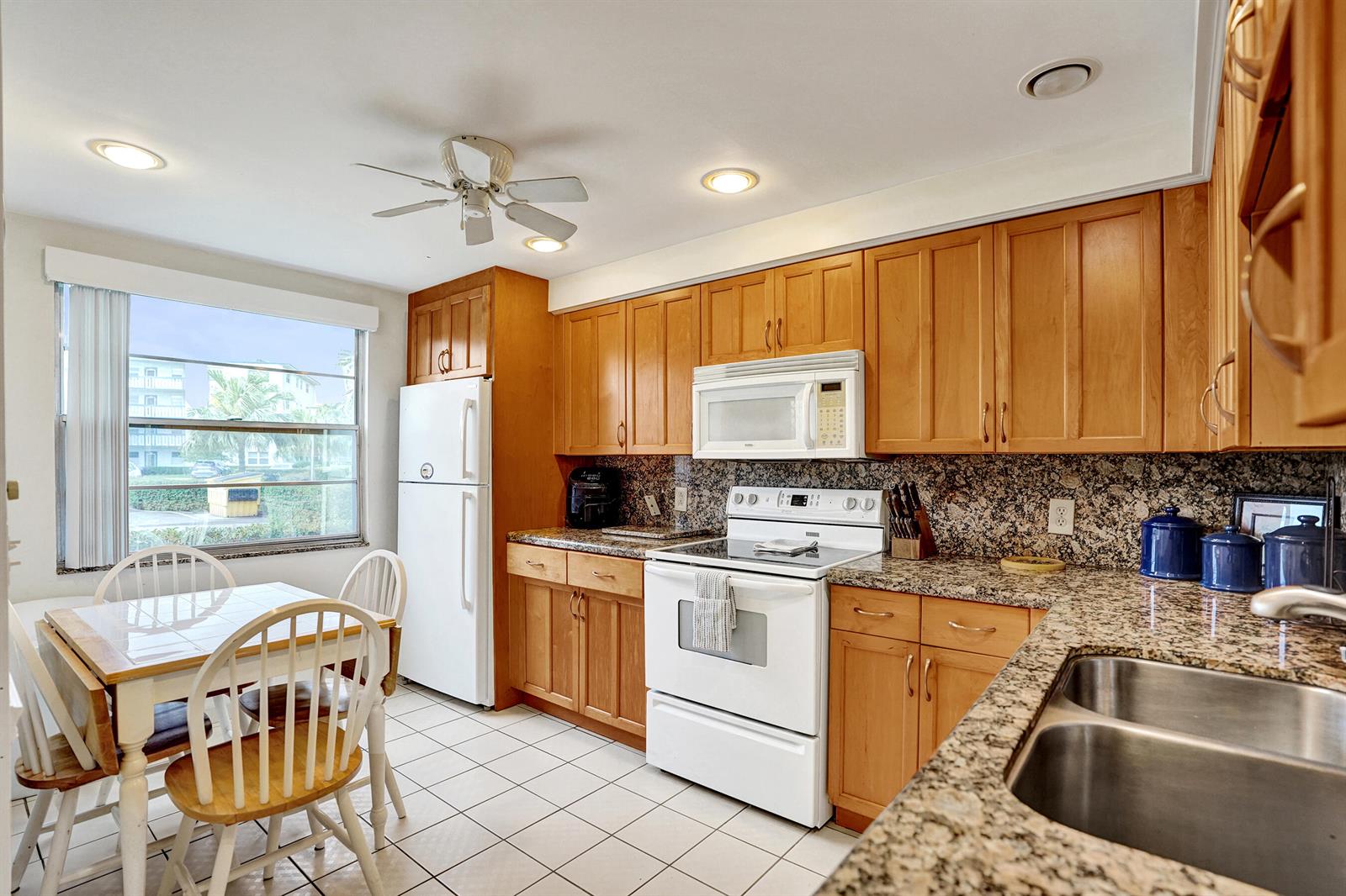 A kitchen with wood cabinets, granite countertops, white appliances, and a small dining area — 1020 Lincoln, Boca Raton FL 33434, BOCA RATON, FL