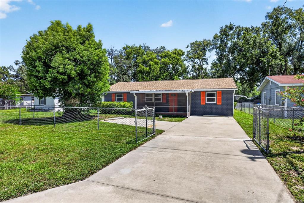 A gray brick house with orange shutters and a concrete driveway sits behind a fence — 38706 CALVIN AVENUE, ZEPHYRHILLS, FL