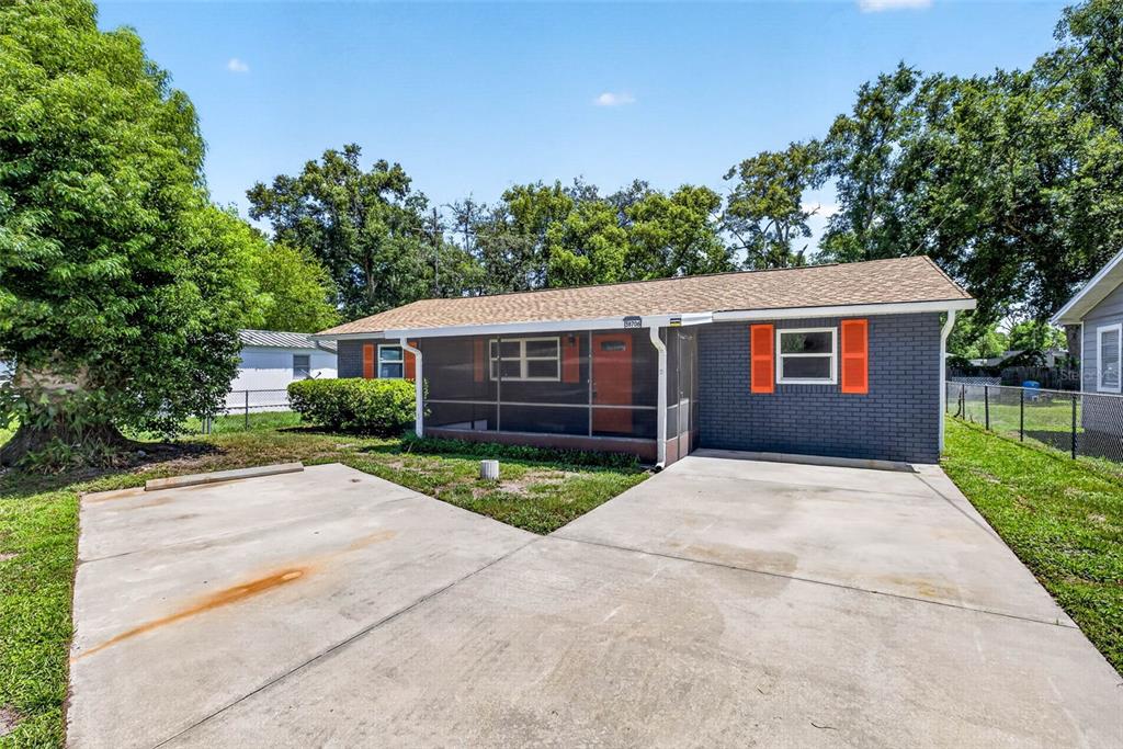 A gray brick house with orange shutters and a screened-in front porch sits behind a driveway — 38706 CALVIN AVENUE, ZEPHYRHILLS, FL