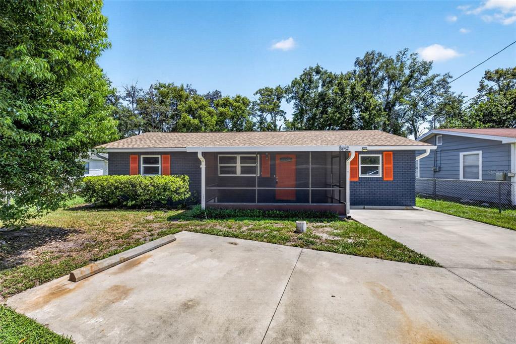 A single-story gray brick house features a screened front porch and bright orange shutters — 38706 CALVIN AVENUE, ZEPHYRHILLS, FL