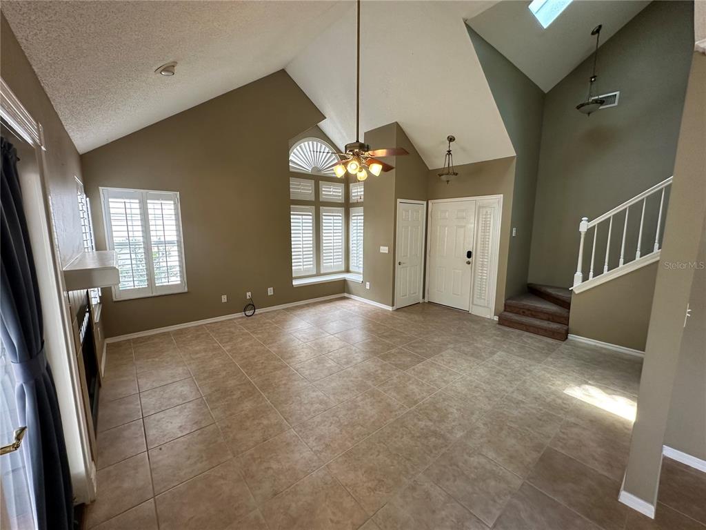 A living room features vaulted ceilings, tile flooring, a ceiling fan, and a staircase — 3837 HOLSTON WAY, ORLANDO, FL