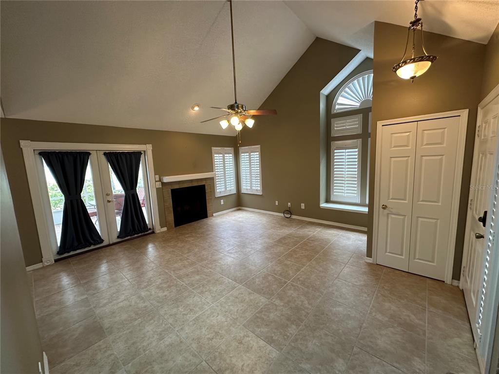 A living room with tile floors, a fireplace, vaulted ceilings, and double glass doors — 3837 HOLSTON WAY, ORLANDO, FL