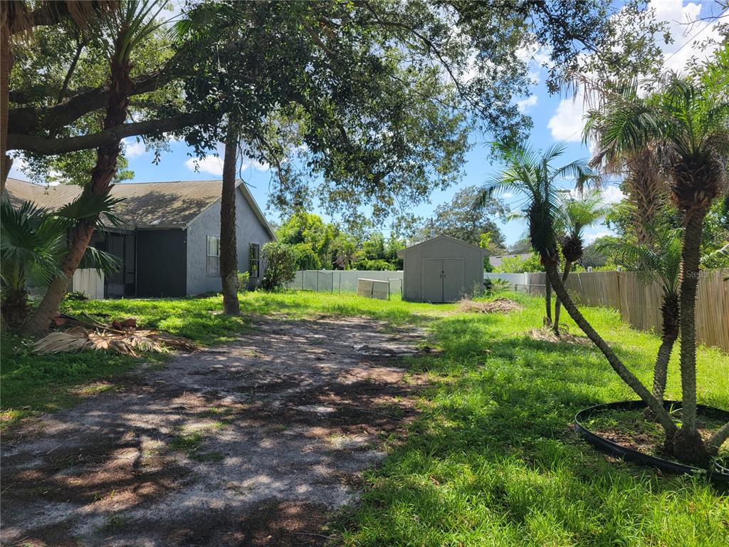 A backyard with a house, a storage shed, trees, and a dirt path — 2218 GRETNA DRIVE, DELTONA, FL
