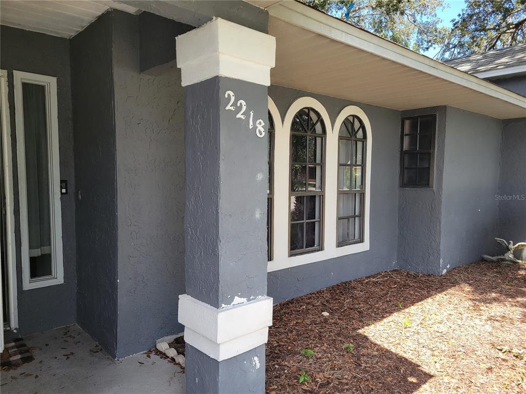A gray stucco house exterior features a front porch pillar with house numbers and windows — 2218 GRETNA DRIVE, DELTONA, FL