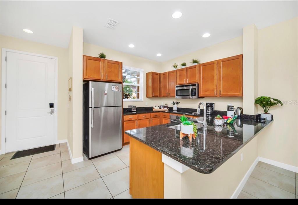 A kitchen features wood cabinets, dark granite countertops, stainless steel appliances, and tile flooring — 2670 CORVETTE LANE, KISSIMMEE, FL