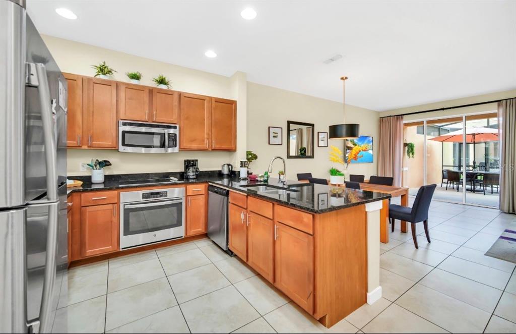 A kitchen with wood cabinets, granite countertops, and stainless steel appliances opens to a dining area — 2670 CORVETTE LANE, KISSIMMEE, FL