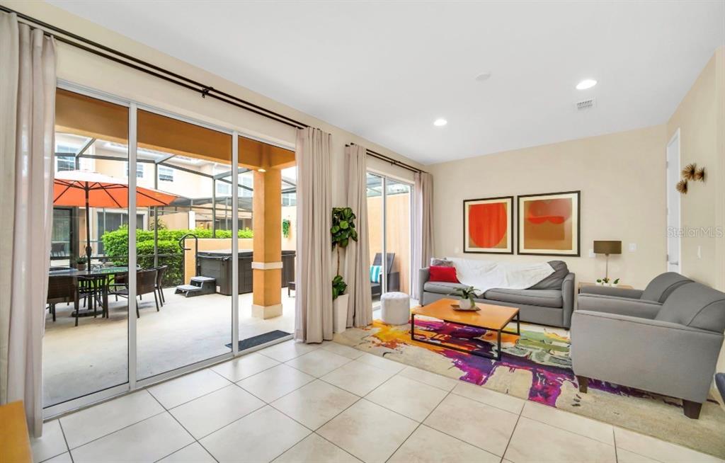 A living room with tile floors, a colorful rug, and sliding doors leading to a patio — 2670 CORVETTE LANE, KISSIMMEE, FL