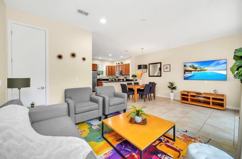 A living room with a colorful rug, two gray armchairs, and an open-concept kitchen — 2670 CORVETTE LANE, KISSIMMEE, FL