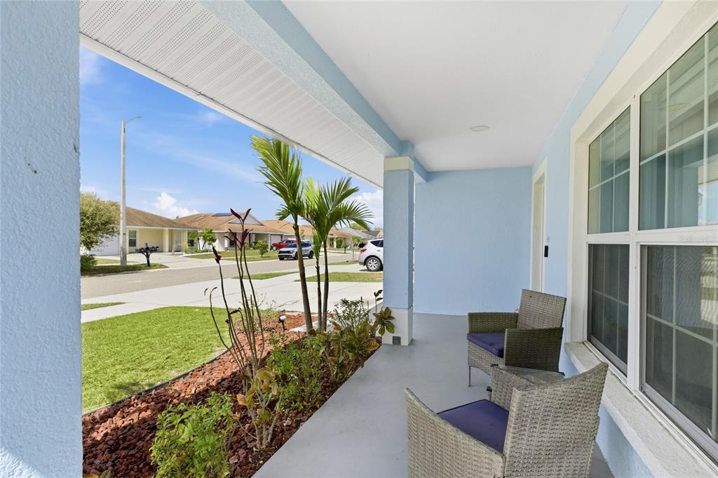 A covered front porch features two wicker chairs, light blue walls, and a landscaped yard — 1202 HUMBLE HAVEN STREET, RUSKIN, FL