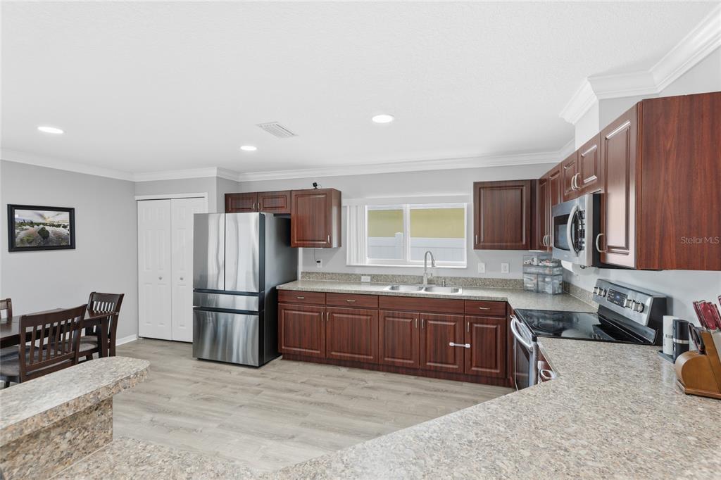A kitchen features dark wood cabinets, stainless steel appliances, and light-colored laminate countertops — 1202 HUMBLE HAVEN STREET, RUSKIN, FL