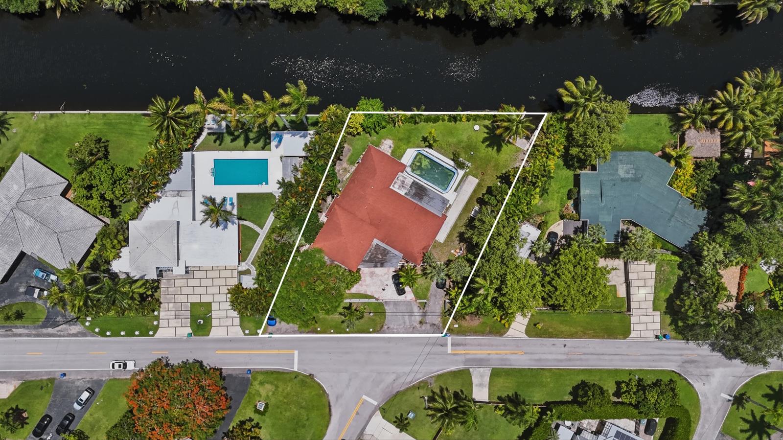 An aerial view shows a house with a red roof, pool, and yard by a canal — 11401 W Biscayne Canal Road, Miami FL 33161, MIAMI, FL