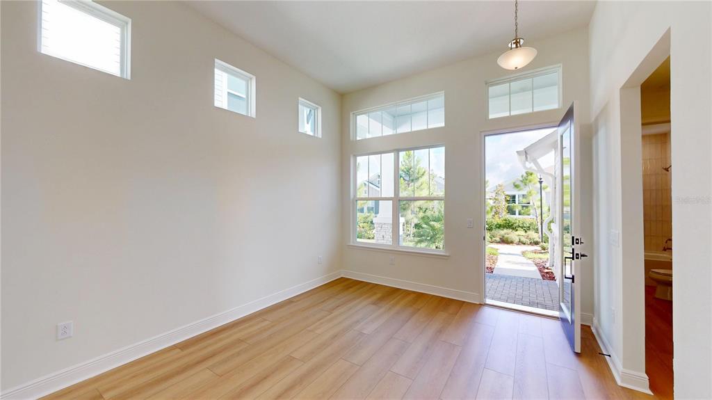 An empty room with light wood flooring, high ceilings, multiple windows, and an open doorway — 28741 JUJUBE ROAD, WESLEY CHAPEL, FL