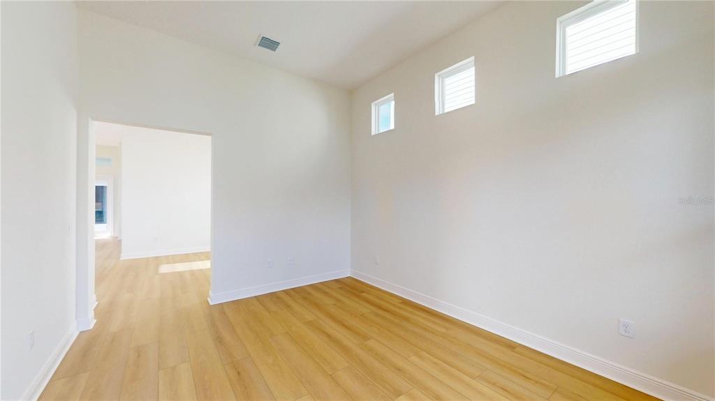 An empty room with light wood flooring, white walls, and three high windows — 28741 JUJUBE ROAD, WESLEY CHAPEL, FL