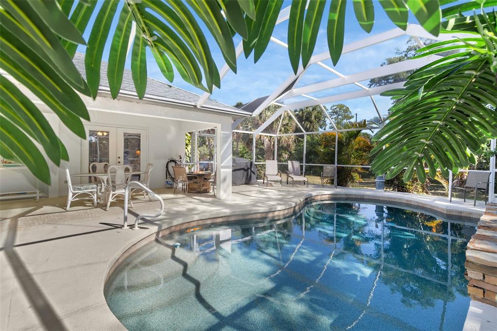 A screened-in patio features a curved swimming pool, outdoor dining area, and tropical landscaping — 4812 KENVIL DRIVE, NORTH PORT, FL
