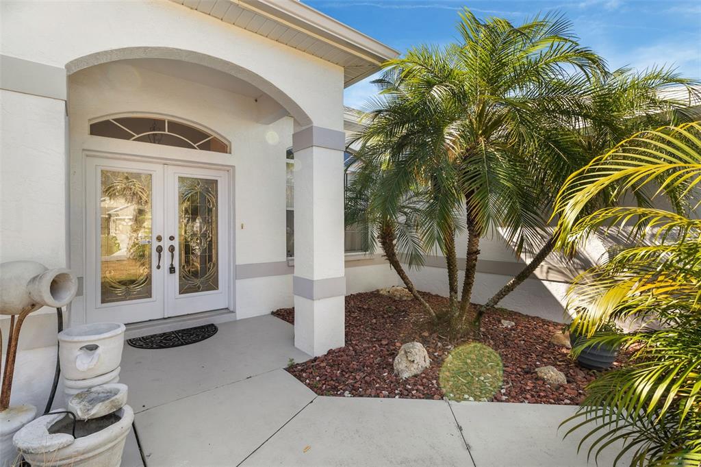The exterior entrance features a white double door, a palm tree, and a stone garden — 4812 KENVIL DRIVE, NORTH PORT, FL