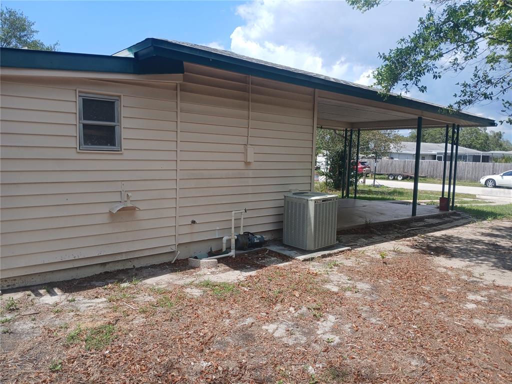 The exterior of a tan house features a covered carport, a window, and an HVAC unit — 7304 ACORN CIRCLE, SPRING HILL, FL