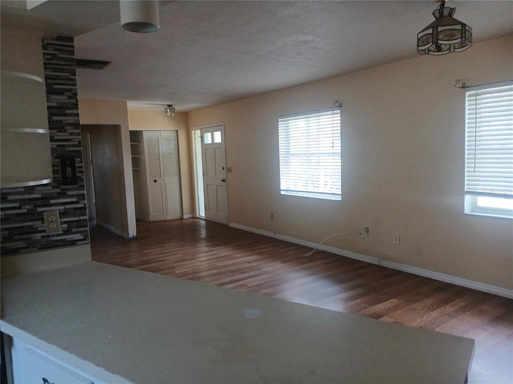 An open-concept living area features wood-look flooring, beige walls, and a tiled kitchen peninsula — 7304 ACORN CIRCLE, SPRING HILL, FL