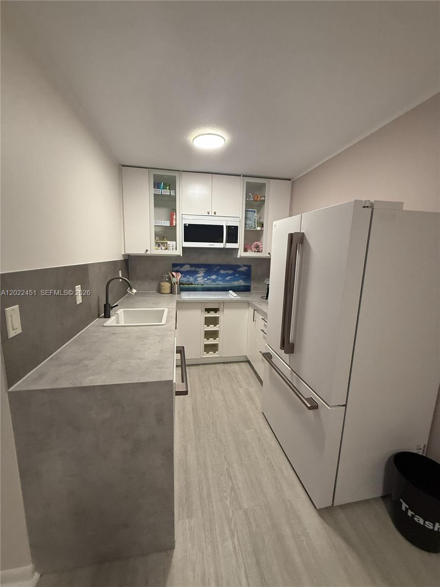 A galley kitchen features white cabinets, grey countertops, a white refrigerator, and light wood flooring — HOLLYWOOD, FL