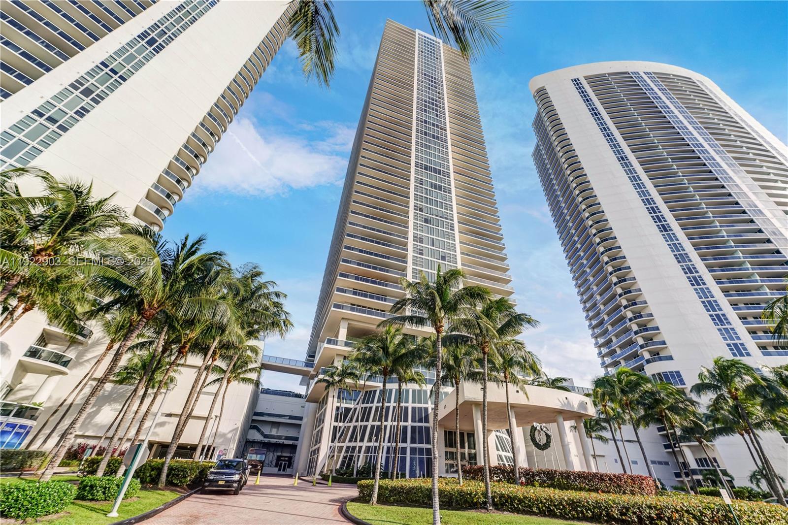 A low-angle view shows three tall, modern residential towers surrounded by palm trees and landscaping — 1830 S Ocean Dr # 3002, Hallandale Beach FL 33009, HALLANDALE BEACH, FL