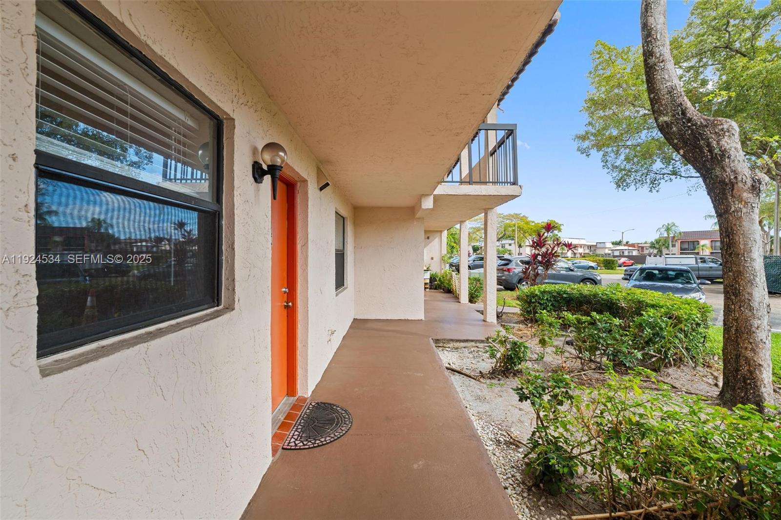 An exterior view of a building walkway with a bright orange door and a balcony — 821 NE 207th Ln # 1, Miami FL 33179, MIAMI, FL