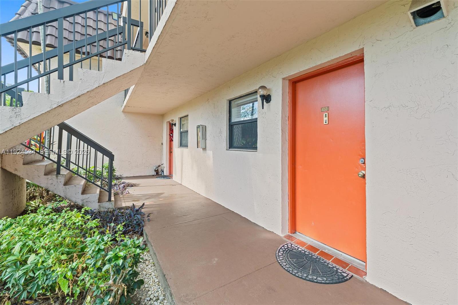 An exterior view of an apartment building walkway featuring orange doors and a concrete staircase — 821 NE 207th Ln # 1, Miami FL 33179, MIAMI, FL