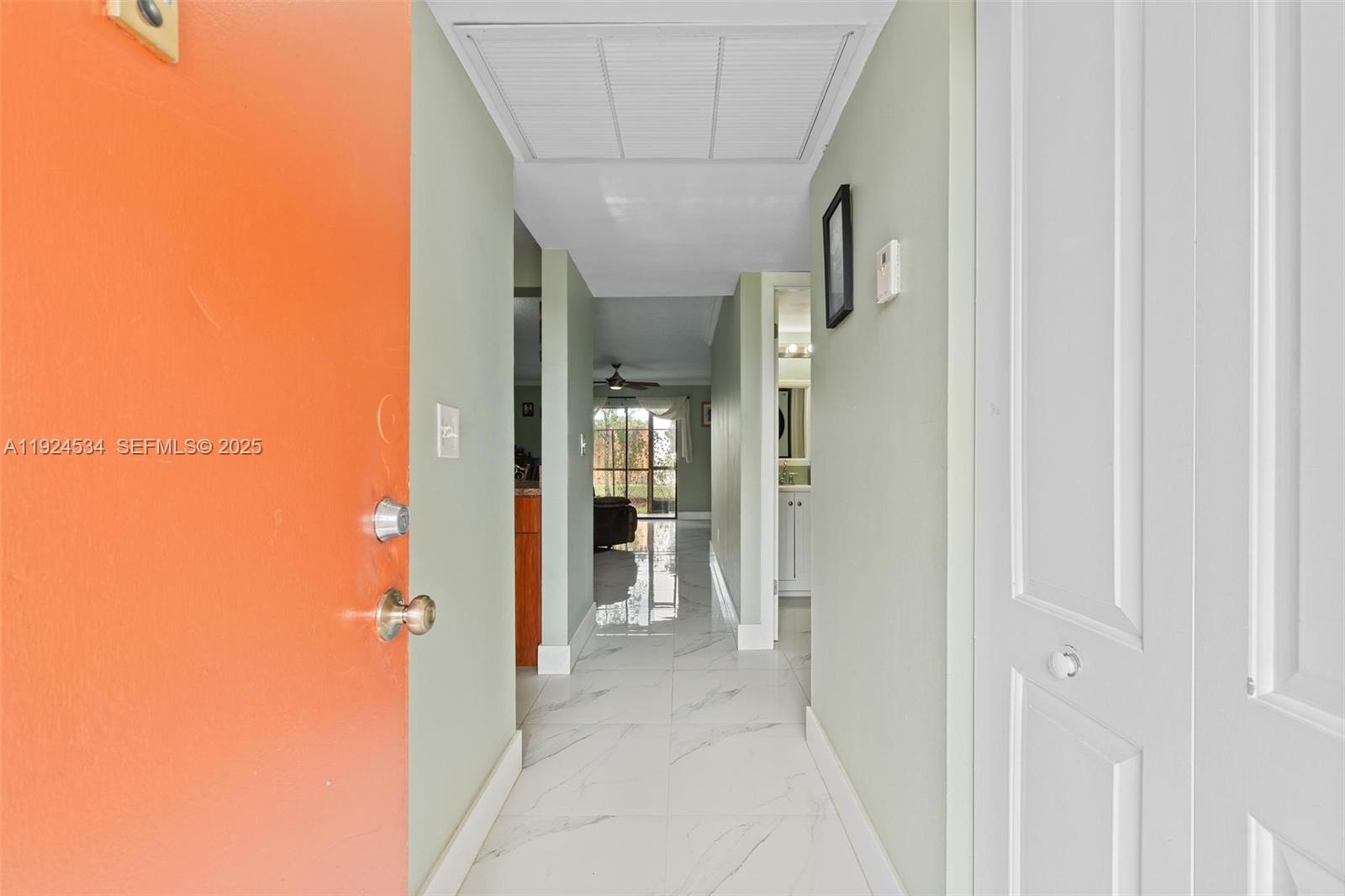 A hallway with white marble-look tile flooring leads toward a bright living area — 821 NE 207th Ln # 1, Miami FL 33179, MIAMI, FL