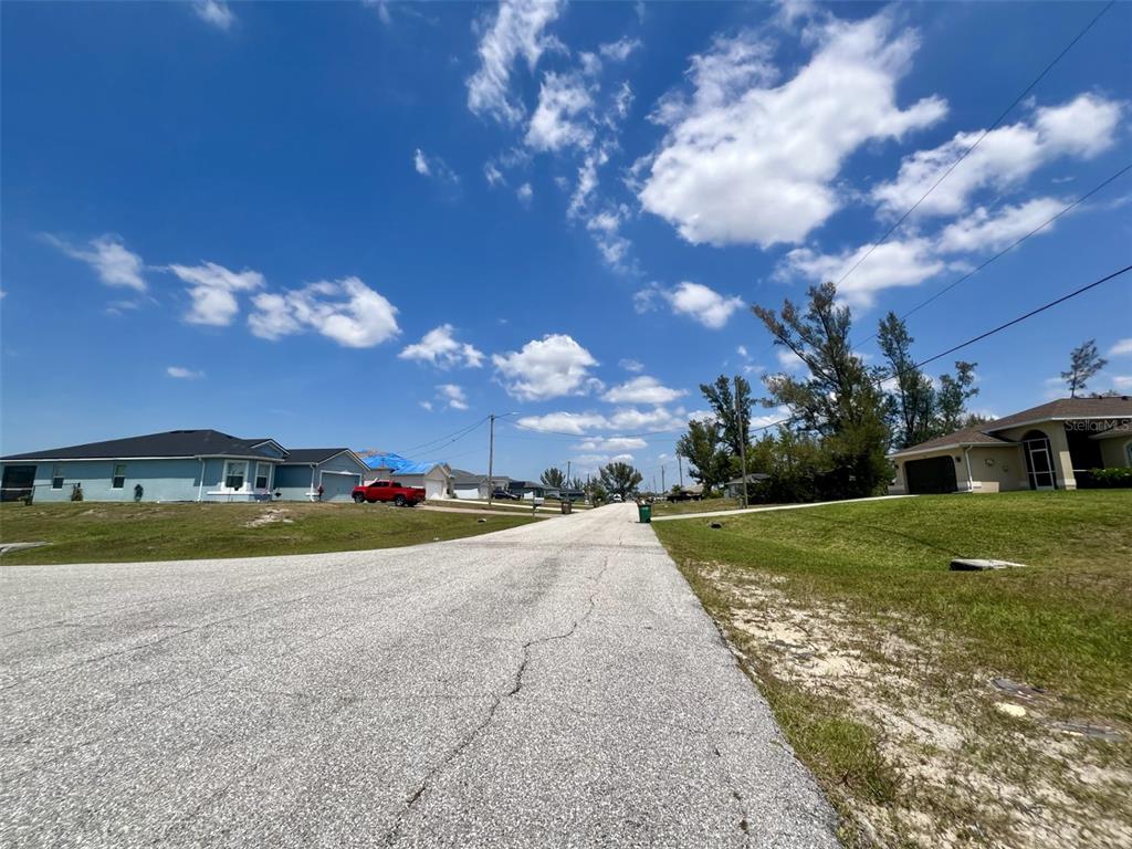 A paved residential street leads toward houses under a bright blue sky with scattered clouds — 1031 NW 20TH PLACE, CAPE CORAL, FL