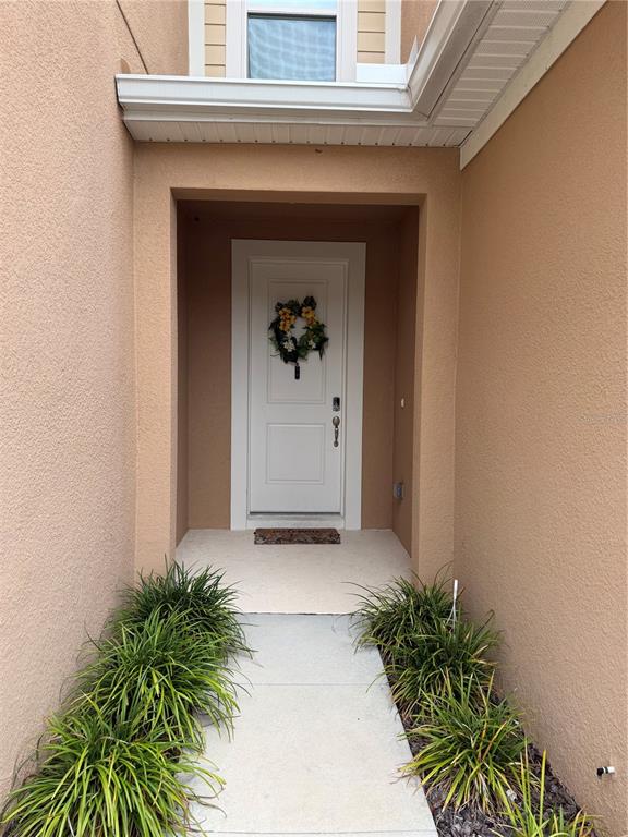 A white front door with a wreath is centered in a recessed entryway with landscaping — 11976 SKY ACRES TERRACE, BRADENTON, FL