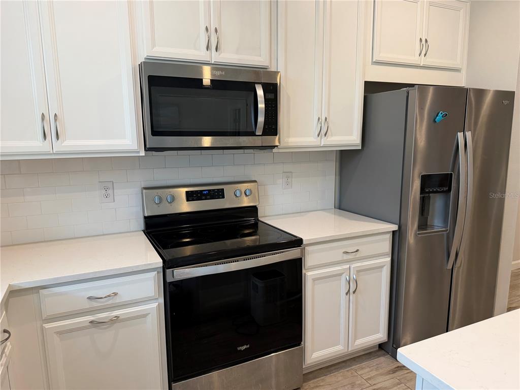 A kitchen features white cabinets, stainless steel appliances, and a white subway tile backsplash — 11976 SKY ACRES TERRACE, BRADENTON, FL