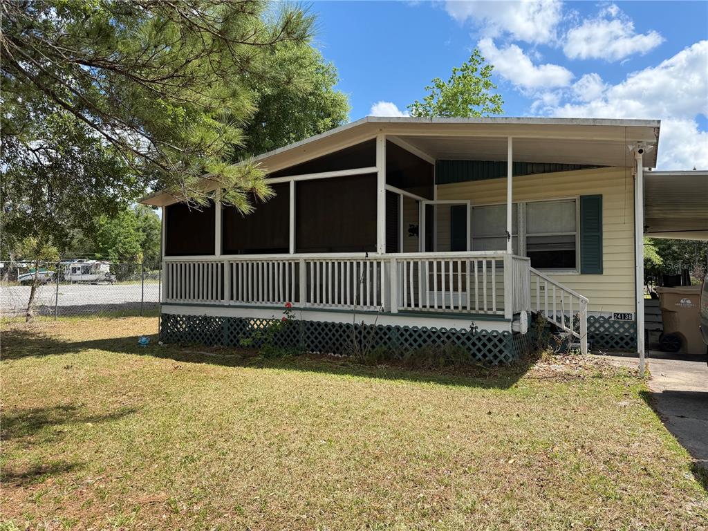 A single-story mobile home features a screened-in front porch, white railings, and lattice skirting — 24138 PANTHER ROAD, ASTOR, FL