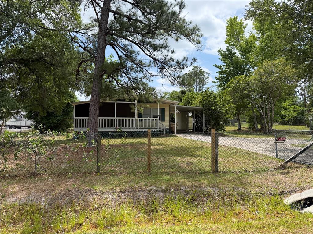 A yellow mobile home with a screened porch sits behind a chain-link fence — 24138 PANTHER ROAD, ASTOR, FL