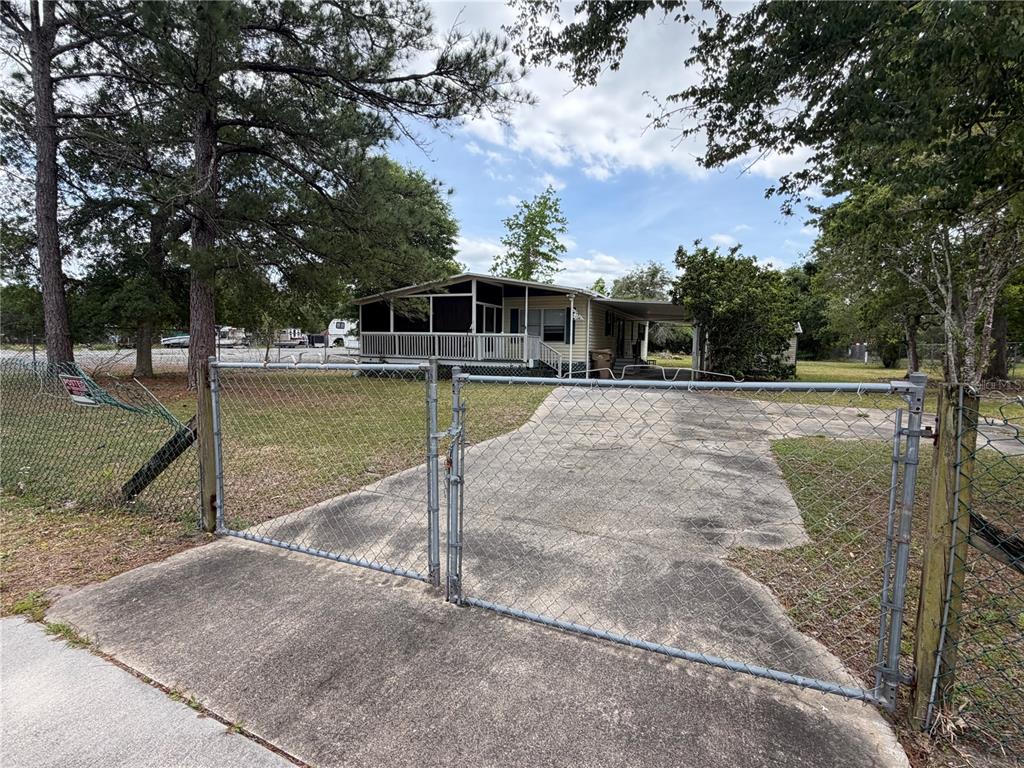 A chain-link fence and gate open to a concrete driveway leading to a mobile home — 24138 PANTHER ROAD, ASTOR, FL