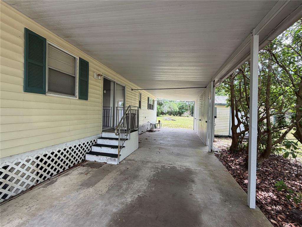 A yellow mobile home features a concrete carport and a set of stairs leading inside — 24138 PANTHER ROAD, ASTOR, FL