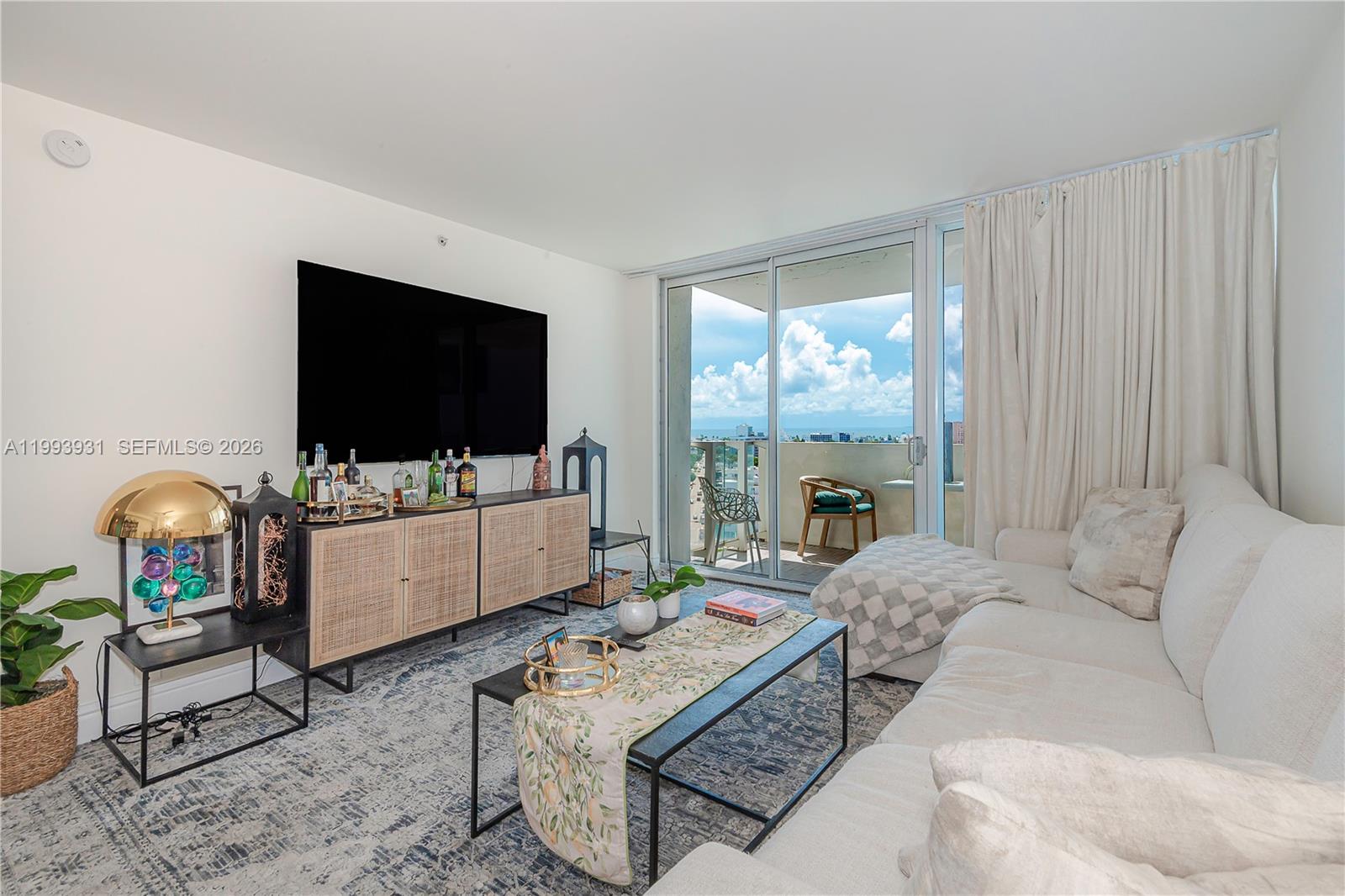 A living room features a large television, a white sofa, and a balcony with ocean views — 1100 West Ave # 1427, Miami Beach FL 33139, MIAMI BEACH, FL