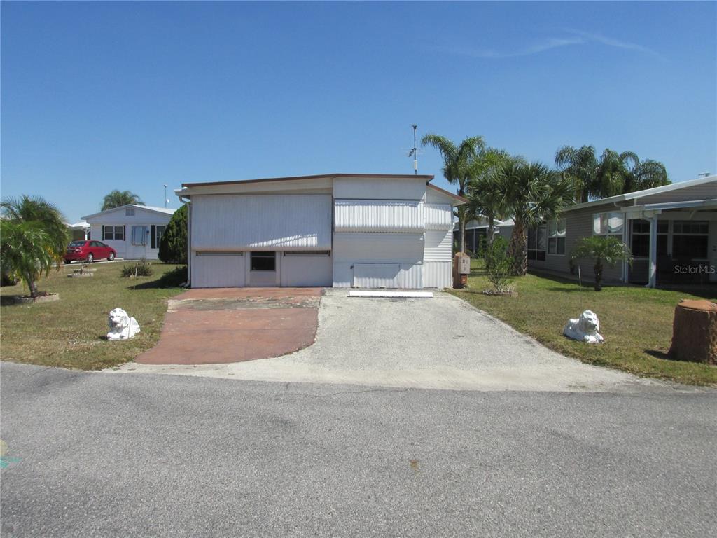 A single-story manufactured home features a white exterior, a driveway, and two decorative lion statues — 10 RED QUILL CIRCLE, LAKE WALES, FL
