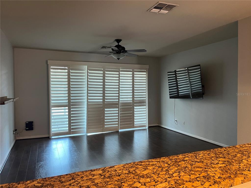 A living room features dark hardwood floors, plantation shutters on sliding doors, and a wall-mounted television — 4971 SW 45TH STREET UNIT na, OCALA, FL