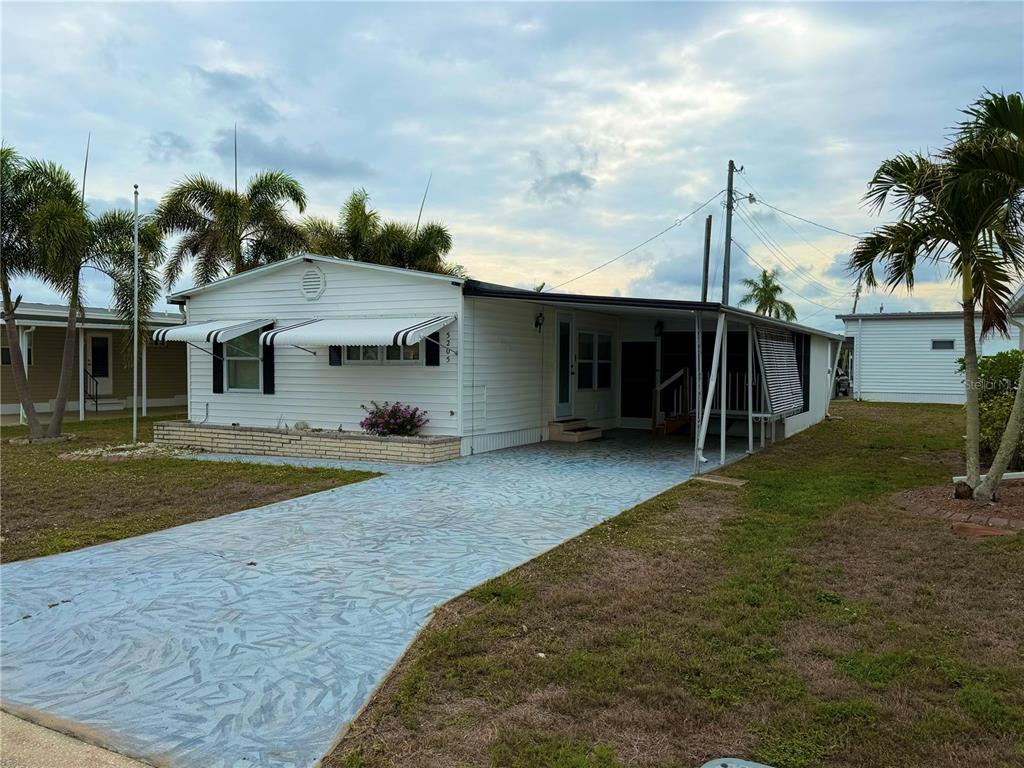 A white single-story manufactured home features a painted driveway, a carport, and palm trees — 5205 5TH STREET E, BRADENTON, FL