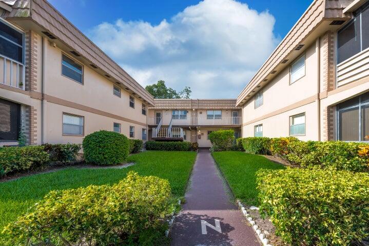 A courtyard between two multi-story apartment buildings features a central walkway and manicured landscaping — 657 Brittany N, Delray Beach FL 33446, DELRAY BEACH, FL