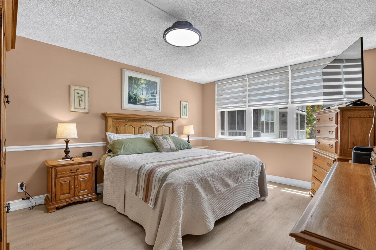 A bedroom features a wooden bed frame, light-colored flooring, and a large window with blinds — 2809 Florida Boulevard # 208, Delray Beach FL 33483, DELRAY BEACH, FL