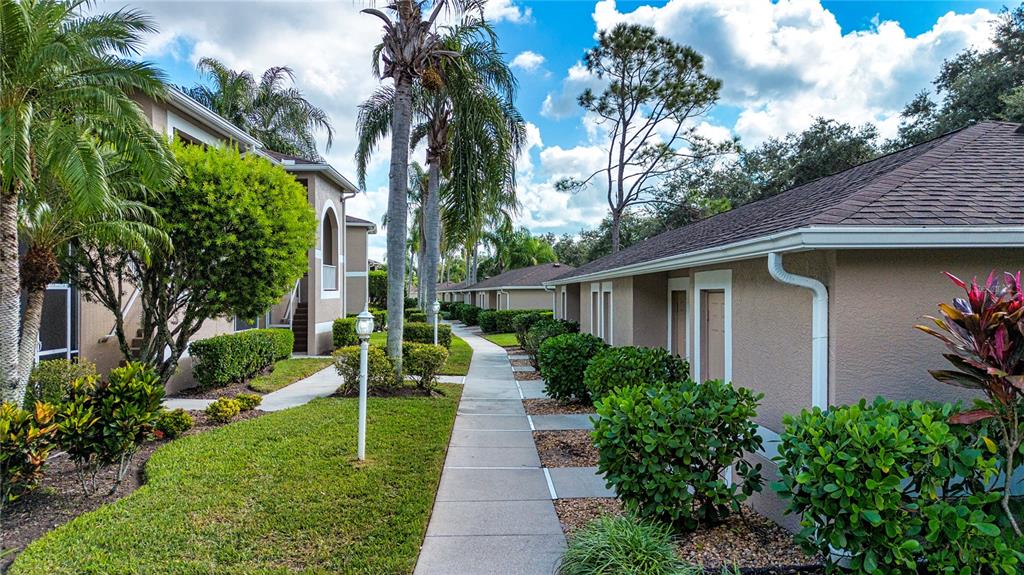 A paved walkway leads between two tan apartment buildings surrounded by palm trees and landscaping — 5300 HYLAND HILLS AVENUE UNIT U2016, SARASOTA, FL