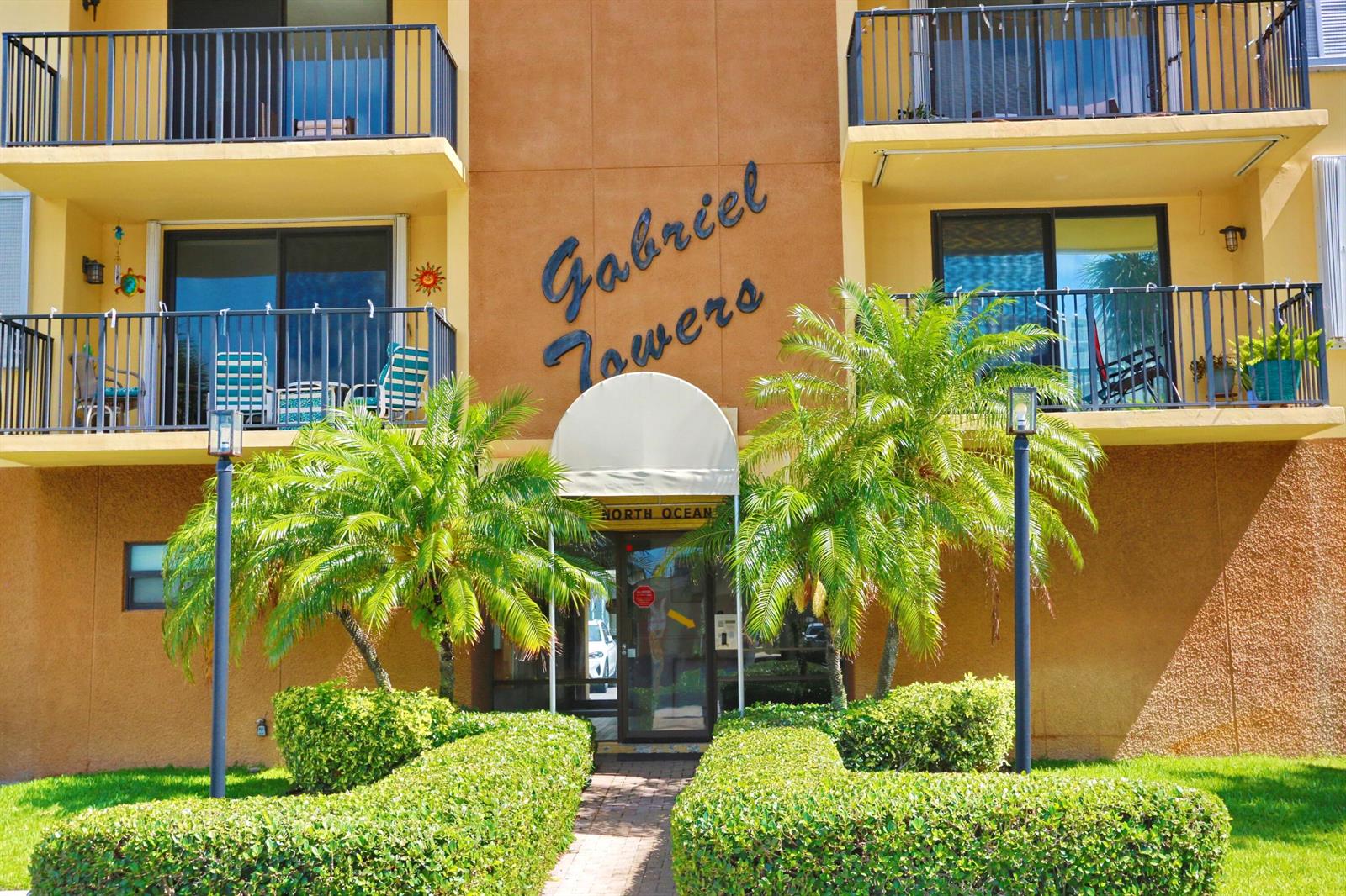The exterior of a multi-story apartment building features a central entrance, balconies, and palm trees — 801 N Ocean Boulevard # 803, Pompano Beach FL 33062, POMPANO BEACH, FL