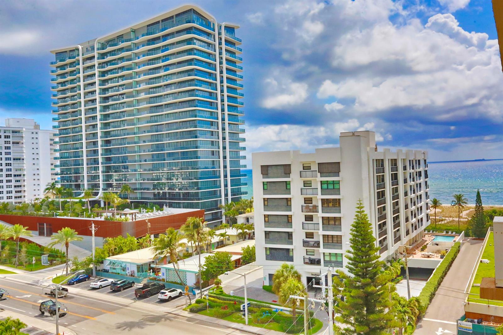 An exterior view shows a tall glass residential tower next to a smaller white apartment building — 801 N Ocean Boulevard # 803, Pompano Beach FL 33062, POMPANO BEACH, FL
